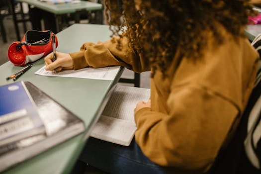 Student in a classroom writing on a test paper, studying.